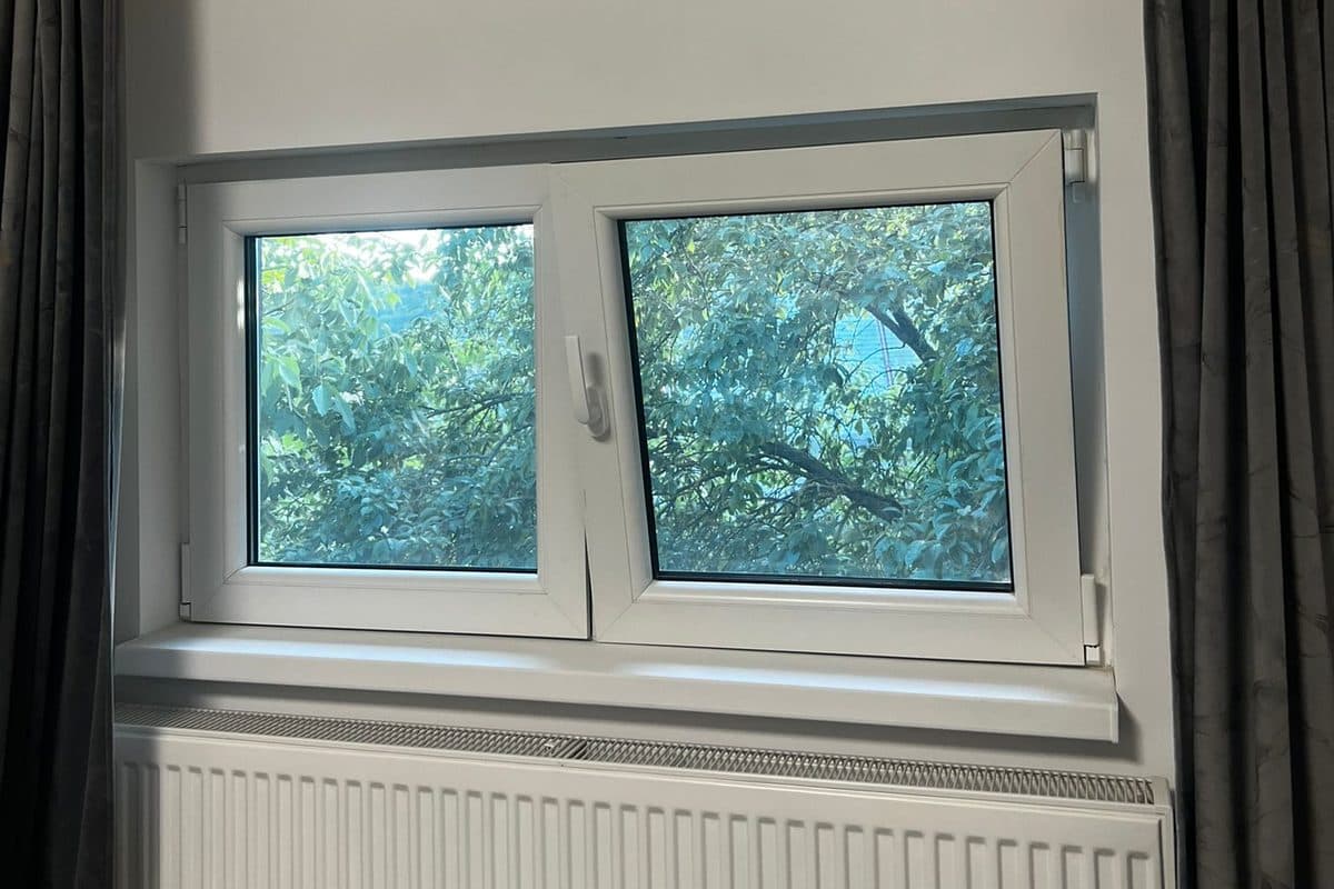 Fereastra termopan alba din PVC cu doua ochiuri, intr-o camera cu draperii gri, fotografiata din interior