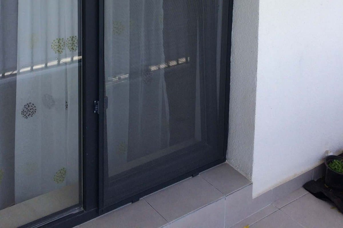 Partea de jos a unei usi de balcon termopan cu plasa de tantari pe balamale: balamaua de jos a plasei si pragul, vazute din exterior